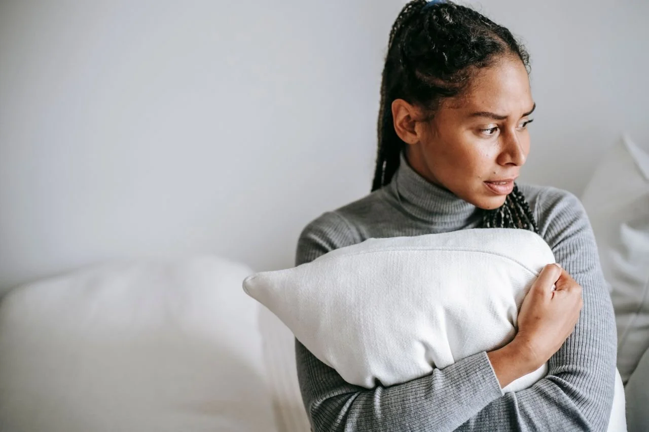 a woman experiencing emotional burnout in a grey sweater holds a pillow