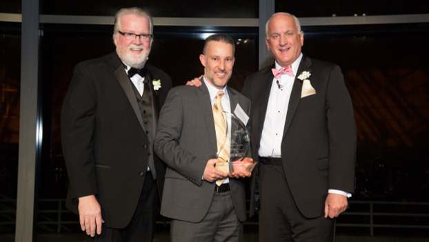 Coachman Square at Woodbridge Dining Services Director Christopher Raymond , center, accepts the Navigation Award for his community from Bob Moran and Tom.