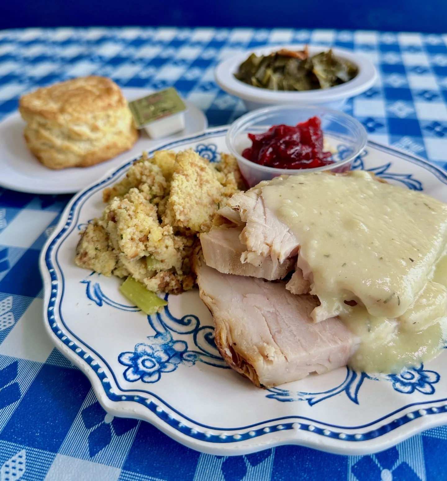 Turkey Feast plate with sliced turkey and gravy, cornbread dressing, cranberry sauce, collard greens, and a buttermilk biscuit