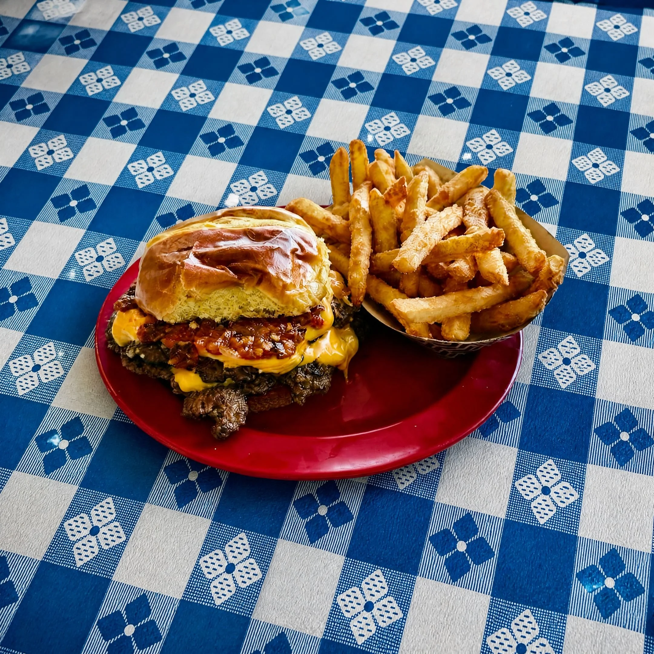 Double smash burger with melted American cheese and tomato bacon jam on a brioche bun, with french fries on a red plate