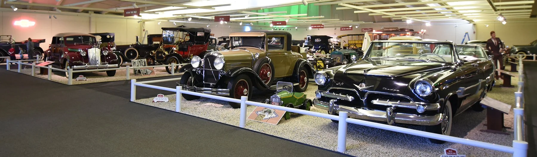 A collection of vintage cars displayed in a museum exhibit with signs and barriers around them.