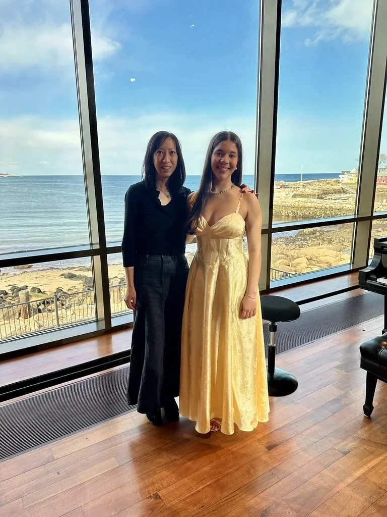 Piano teacher Anita Yu with a student at a recital, oceanfront venue with a grand piano