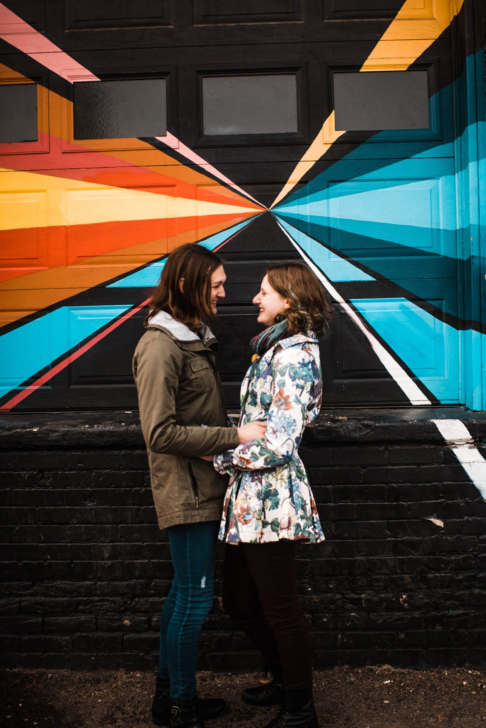 Lesbian couple cuddling in front of a RiNo art mural, Denver Colorado RiNo art mural, RiNo Arts District, RiNo engagement session, LGBT wedding photographers, LGBT friendly wedding photographers, LGBT engagement photographers, Denver wedding photographers, Denver Engagement photographers