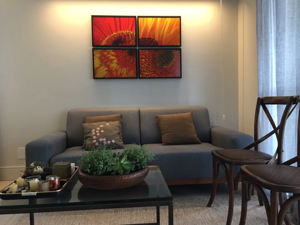 Paredes em tom pastel, cortinas cinza e luminárias em metal branco, fazem a proporção do Metal. O azul do sofá, mais a mesa de vidro, com objetos em preto, trazem a Água. A Madeira está presente nas cadeiras e no arranjo cheio de plantinhas verdes. Fogo e Terra estão nas cores vermelho e laranja das fotografias e na forma quadriculada como foram dispostos os quadros.