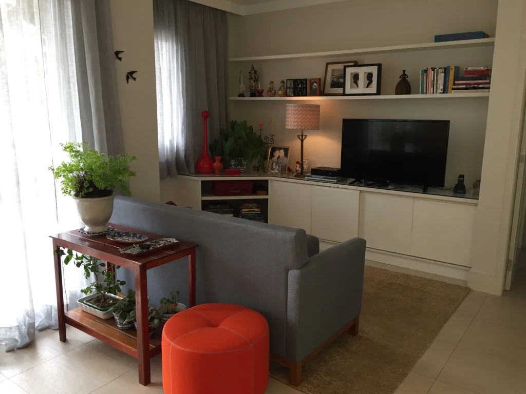 A sala de TV segue a mesma composição de elementos e o pufe laranja ajuda a trazer as pitadas de Terra para o ambiente.