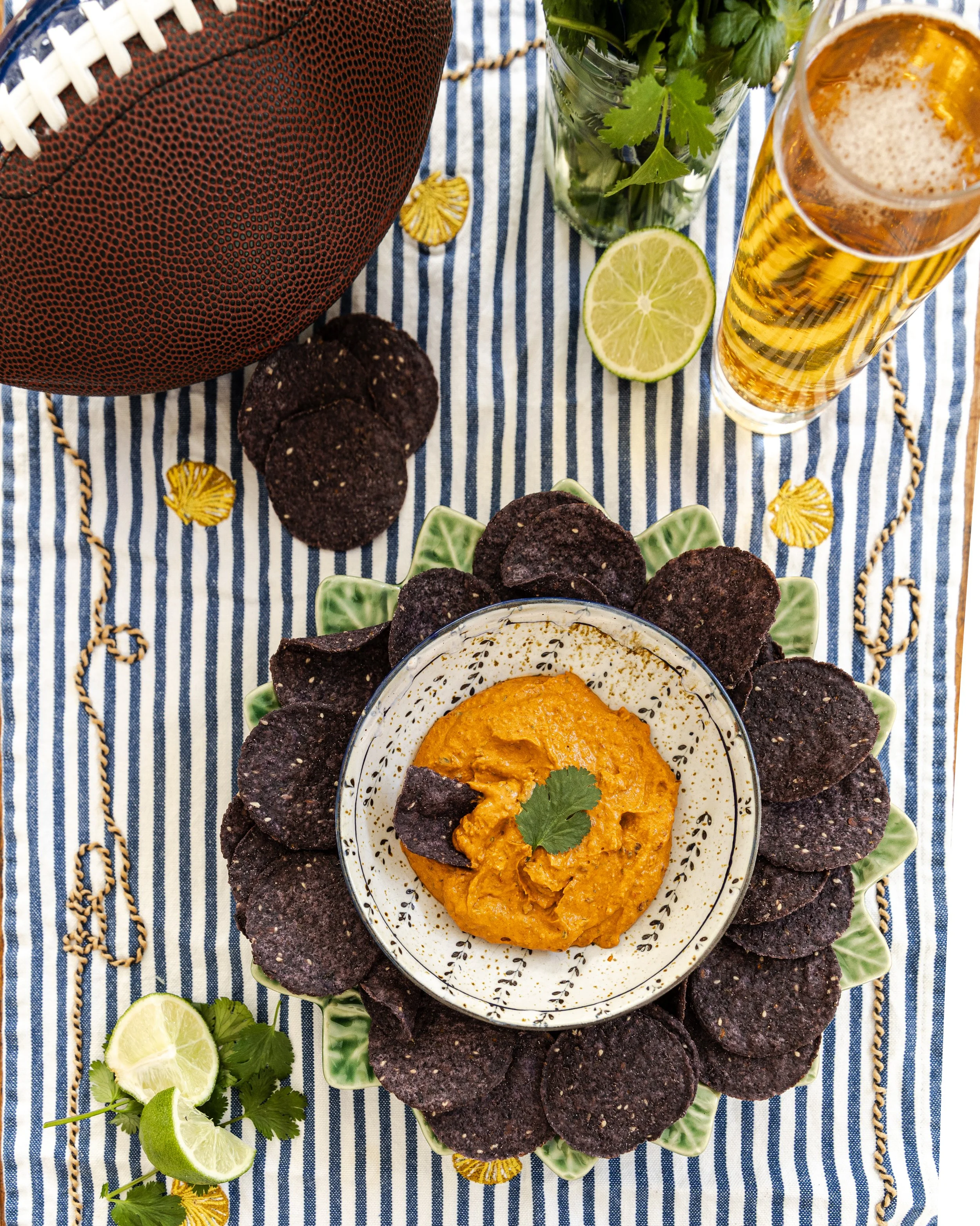 smoky red Chipotle Dip plated in a green plate with blue corn chips. Lime and cilantro surround the plate scene with a cold beer.