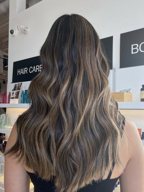 Back of a woman with long, wavy hair styled with highlights in a hair salon.