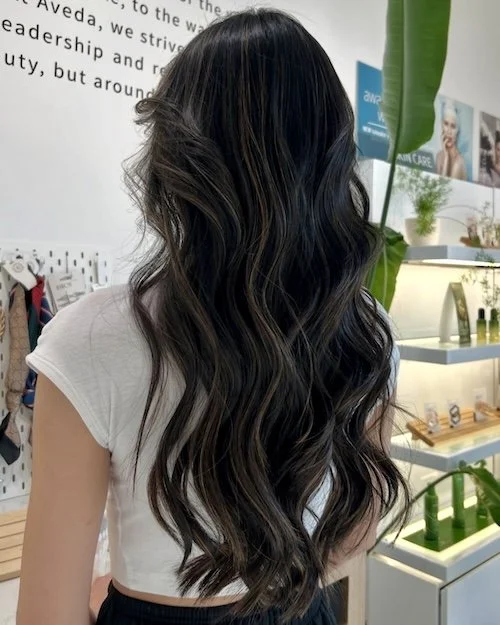 Back view of a woman with long wavy dark brown hair in a retail store.