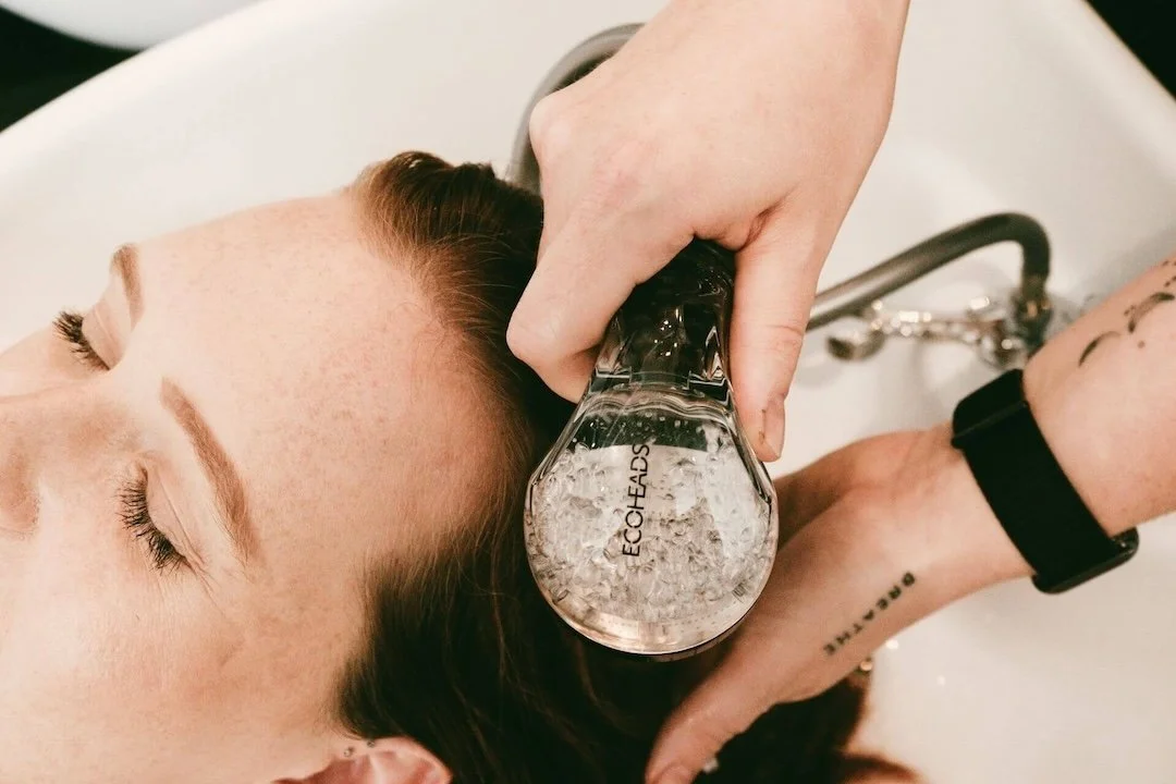 A woman is receiving a scalp treatment with a handheld device that has bubbles, from a person wearing a black watch.