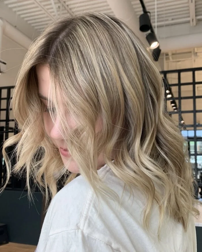Close-up of a woman with shoulder-length blonde, wavy hair in a salon setting.