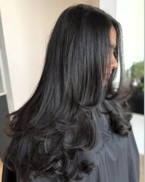Side view of a woman with long, smooth, dark hair in loose curls.