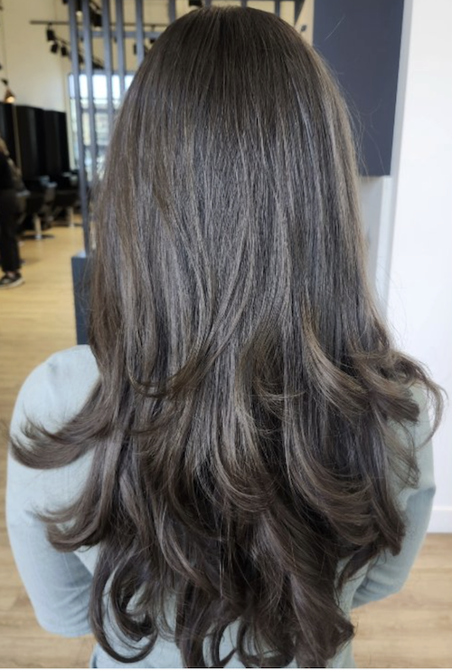 Back view of a woman with long, dark brown wavy hair, indoors, with a modern interior background.