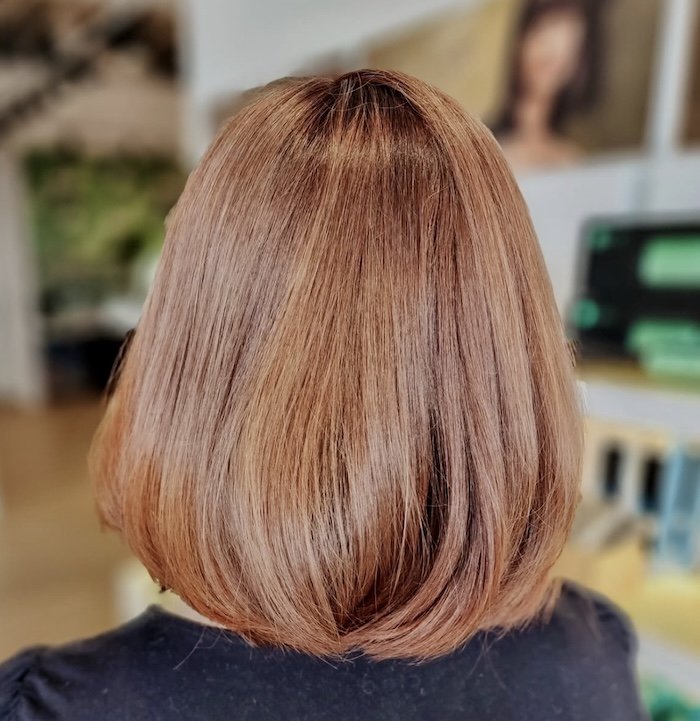 Back view of woman with short, shiny, auburn hairstyle indoors.