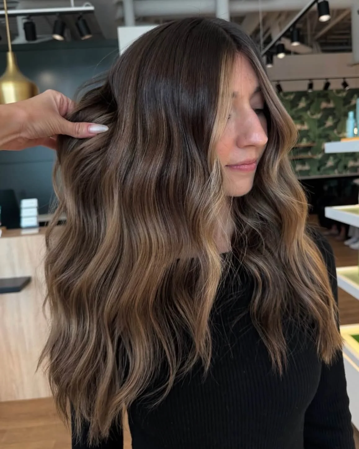 A woman with wavy, multi-tonal brown hair getting her hair done at a salon