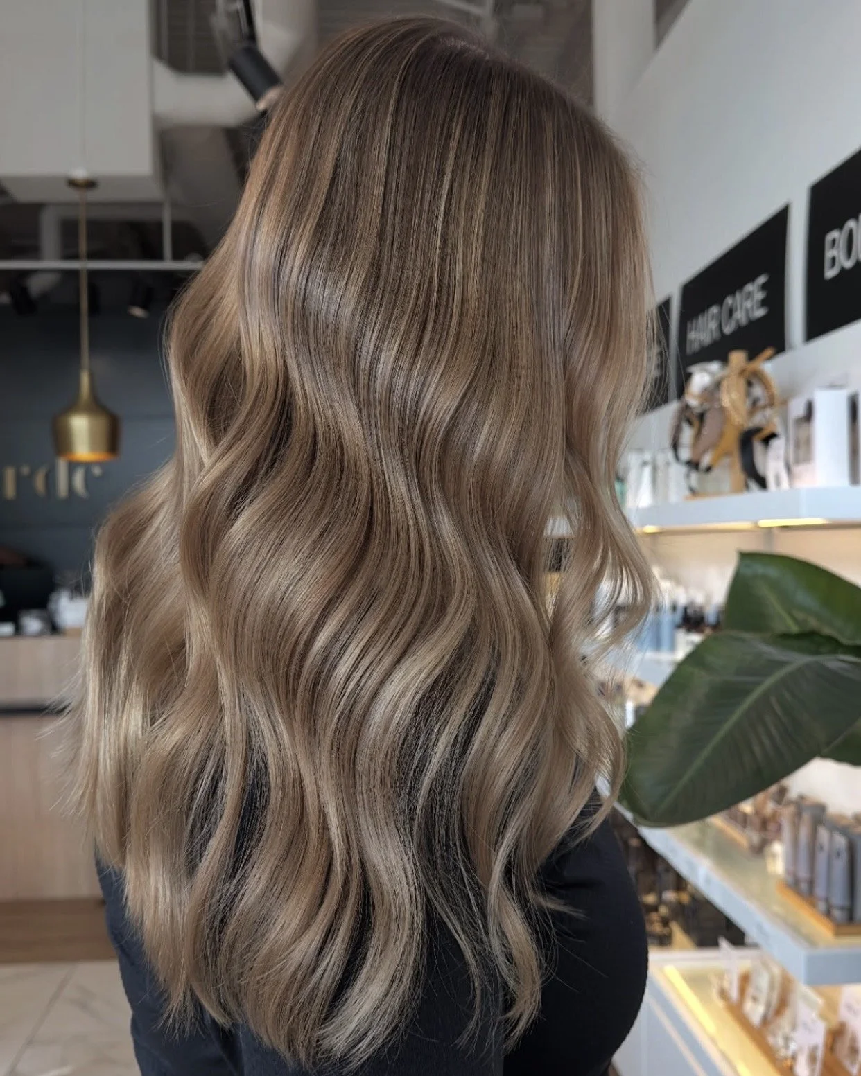 Close-up of a woman's long, wavy blonde hair with darker roots, in a salon setting.