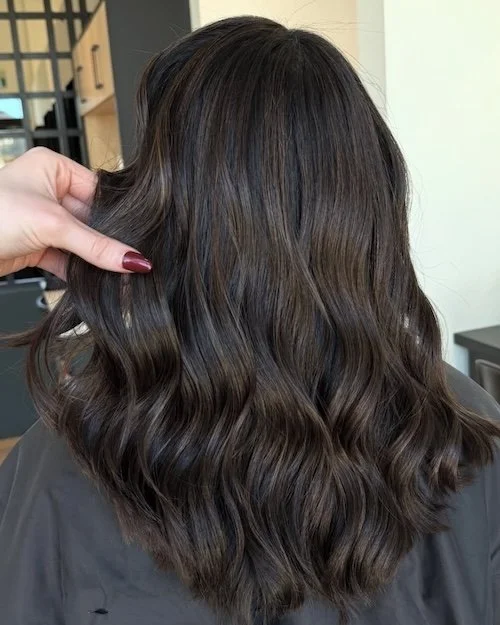 Close-up of a woman's shoulder-length, dark brown hair with soft waves.