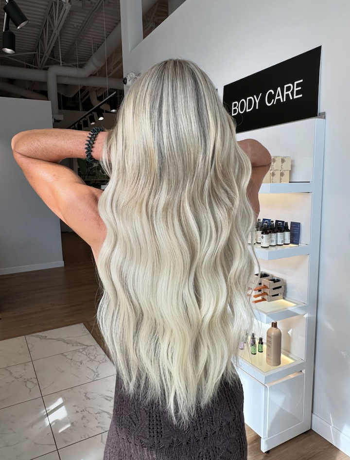 Back view of a woman with long, wavy, platinum blonde hair at a body care section in a store.