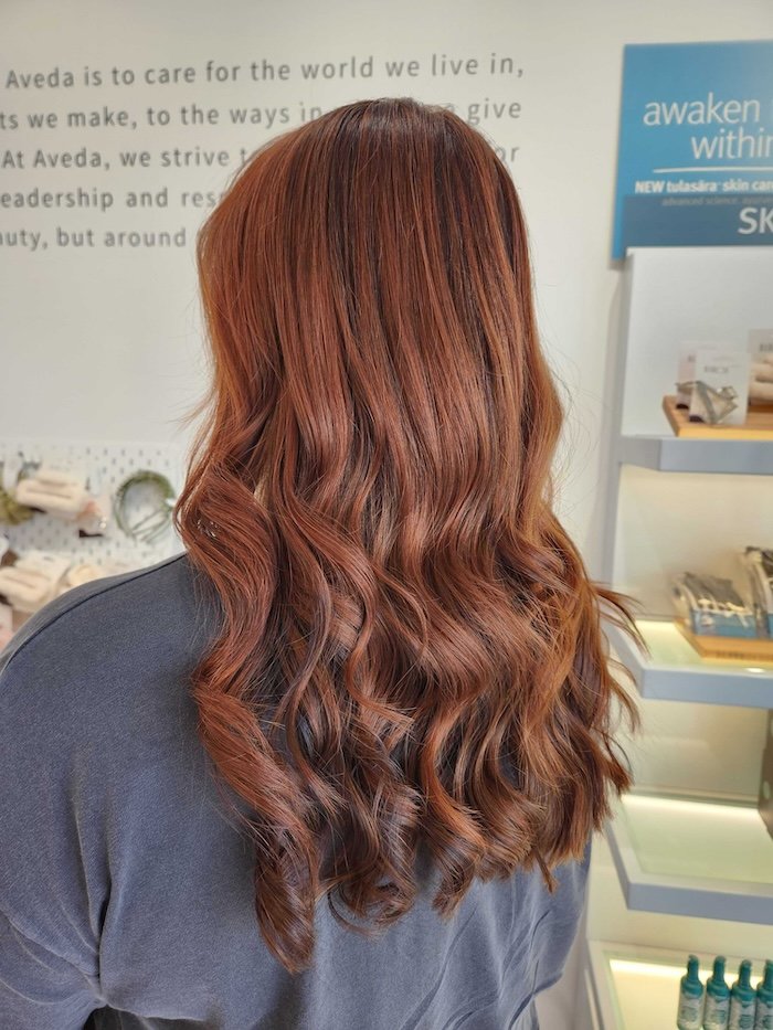 Back of a woman with long, wavy, reddish-brown hair standing in a retail store.