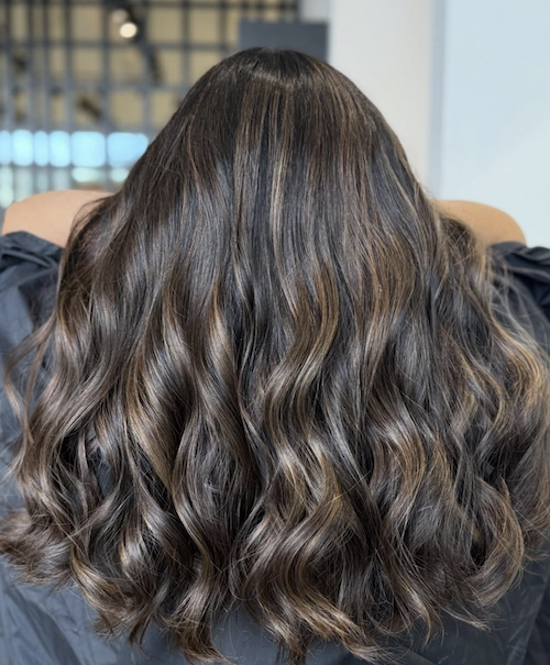 Back of a woman with long, wavy, brown hair with subtle highlights.
