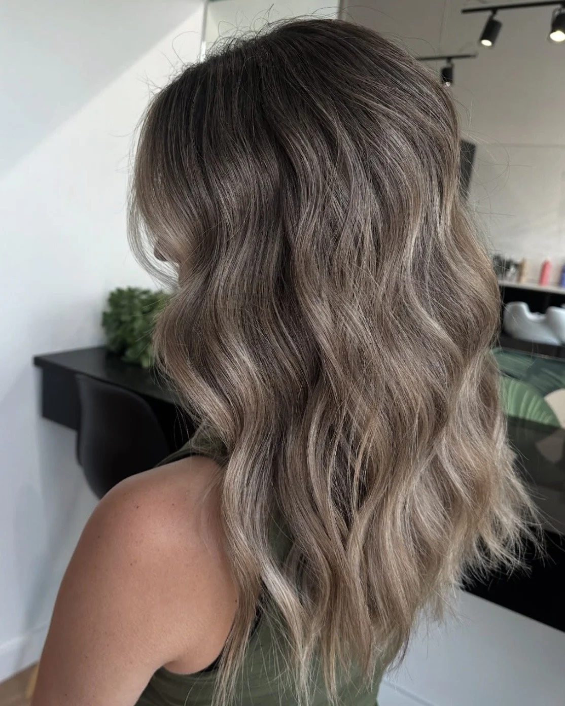 Side view of a woman's wavy, shoulder-length hair with a balayage color technique in shades of light brown and blonde.