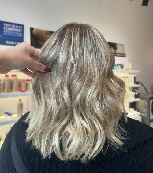 Back view of a woman with shoulder-length blonde wavy hair inside a hair salon