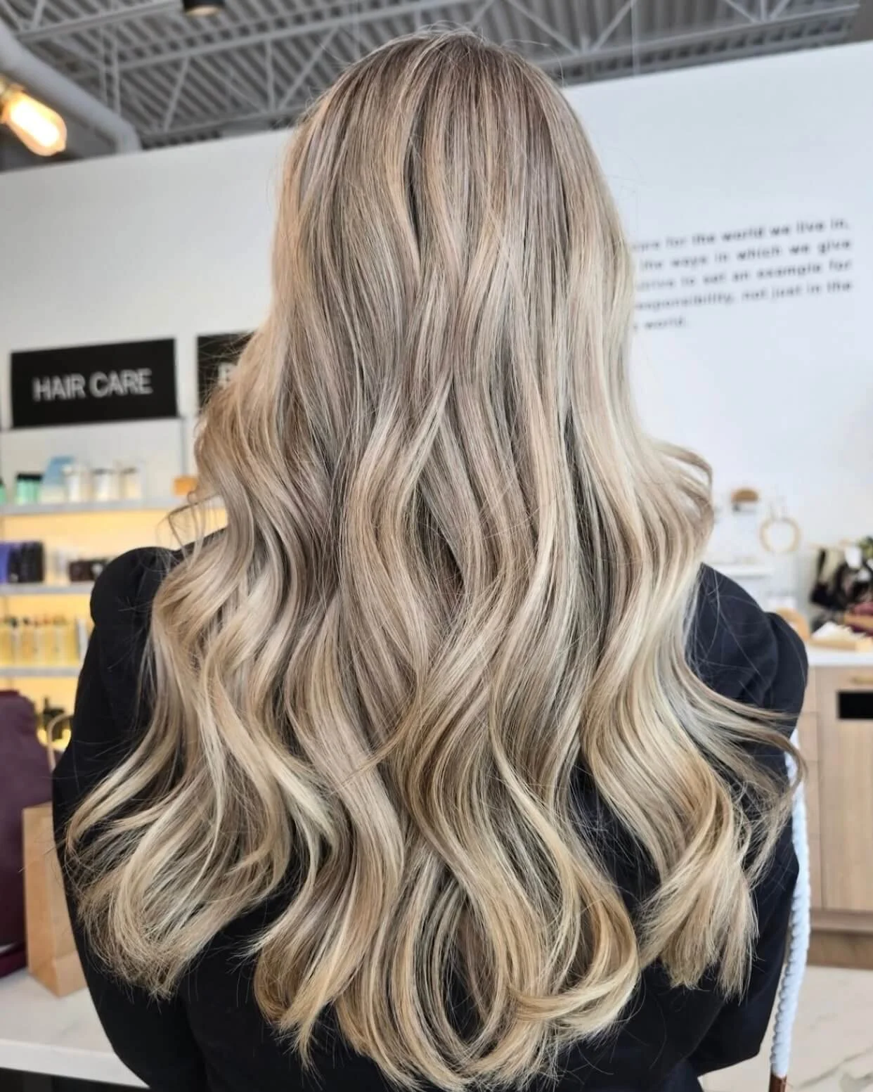 Back view of a woman with long, wavy blonde hair in a salon.