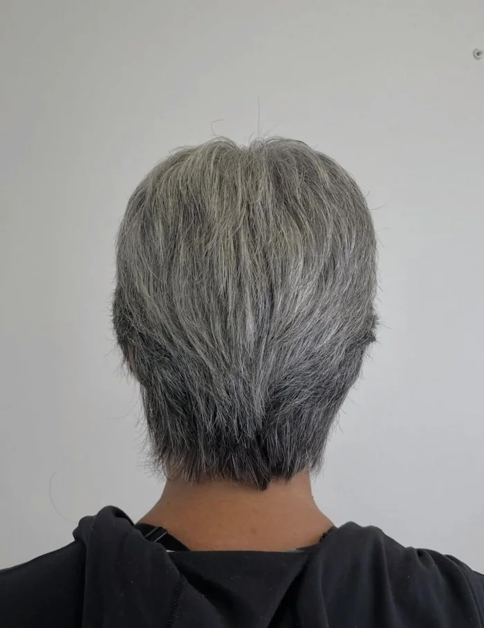 Back of a person with short, gray hair standing against a plain wall.