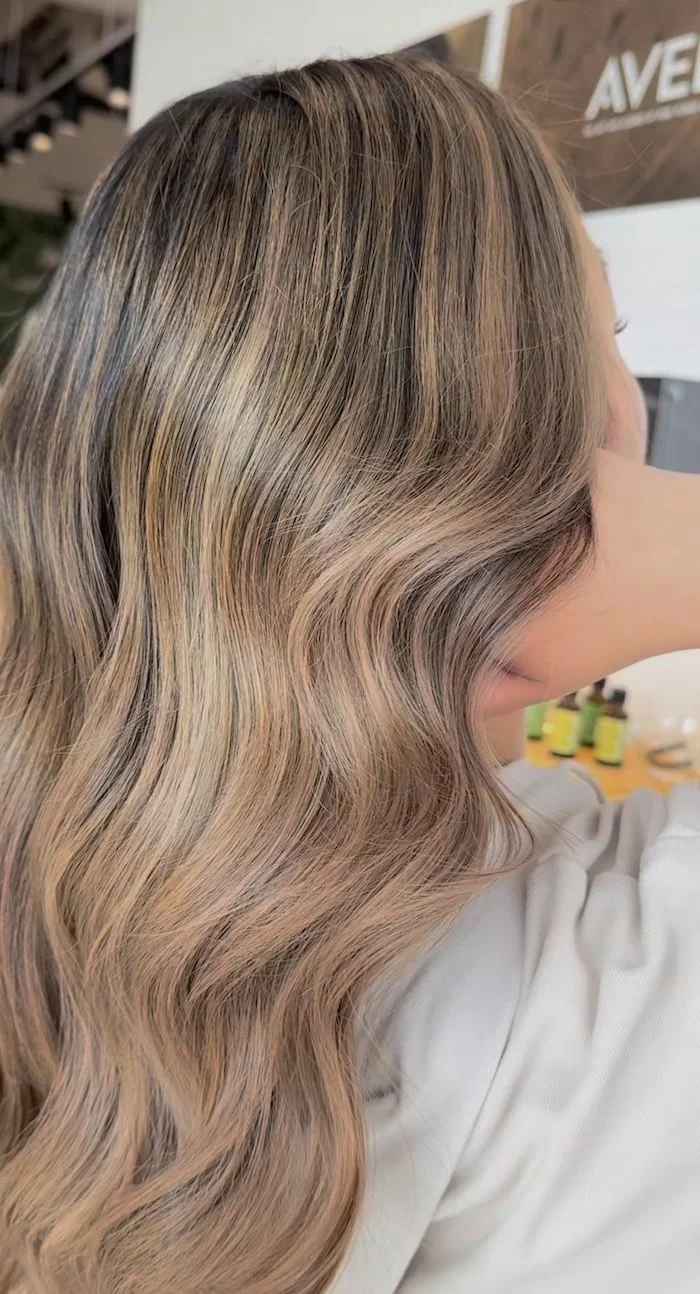 Side view of a woman with long, wavy, blonde hair that has subtle highlights.