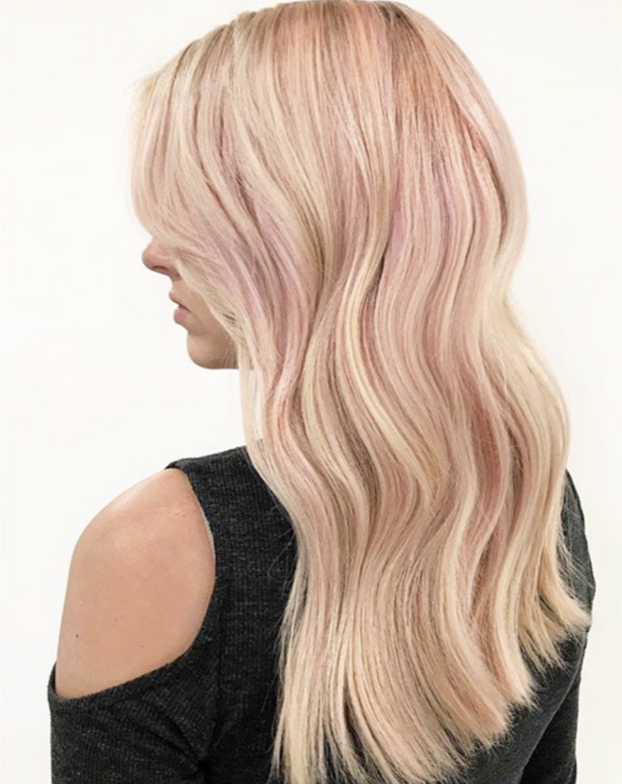 Side view of a woman with long, wavy blonde hair with pink highlights, wearing a black top.