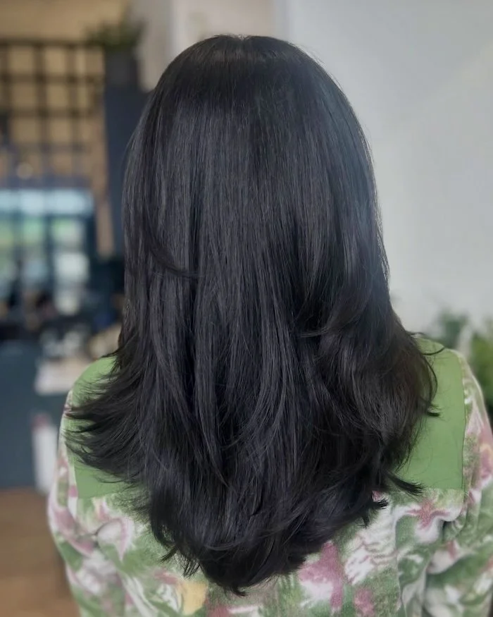 Back of a person with long, shiny, black hair styled with layers and soft waves, wearing a colorful floral shirt.