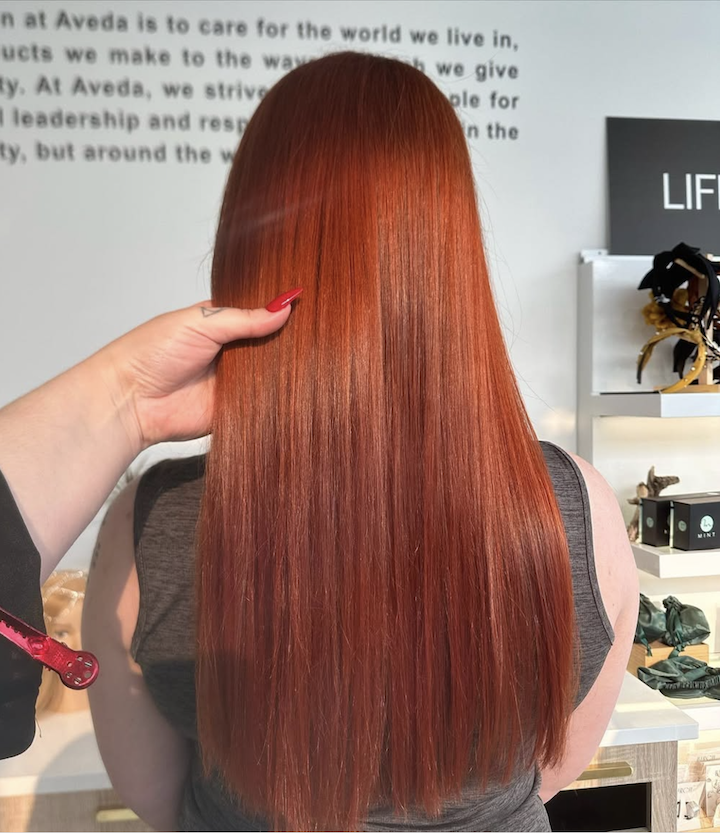 Person with long, straight, vibrant red hair at a hair salon or store inside.