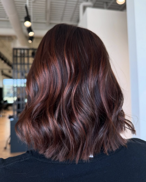 Close-up of a woman's shoulder-length, wavy hair dyed in shades of red and burgundy, taken in a modern hair salon.