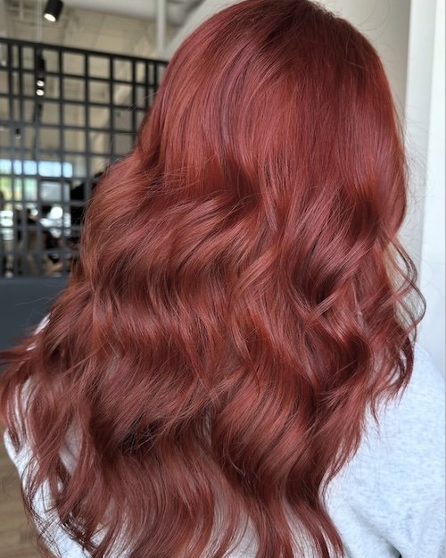 Red wavy hair on a person's back in a salon setting.