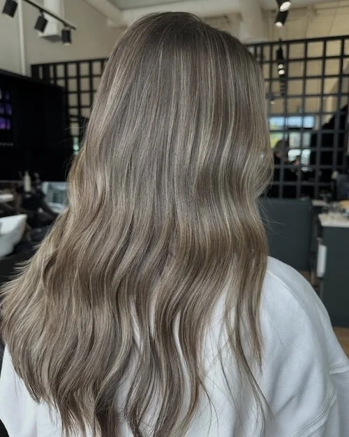 Back of a woman's head showing long, wavy, ash blonde hair in a salon setting.