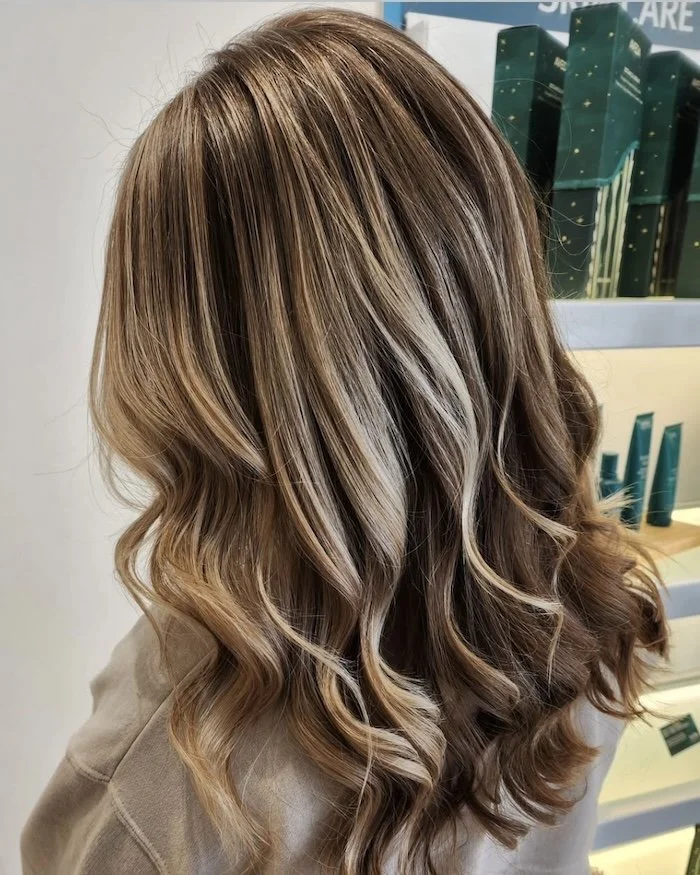 Close-up of a woman's long, wavy, highlighted hair with shades of blonde and light brown, styled in loose curls.