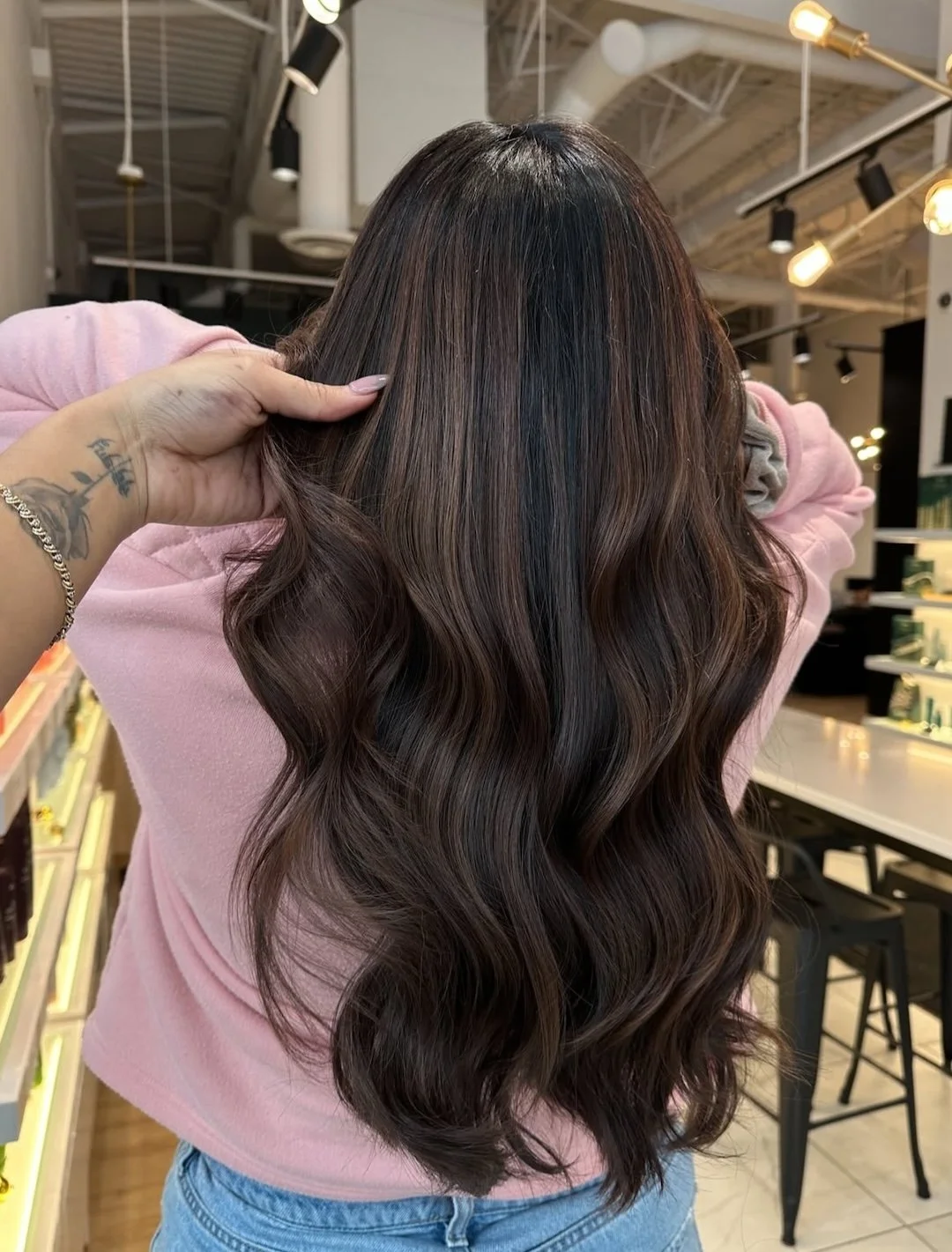 Woman with long, wavy, dark brown hair inside a salon or store.
