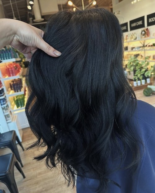 Person with long, wavy black hair being styled in a hair salon.