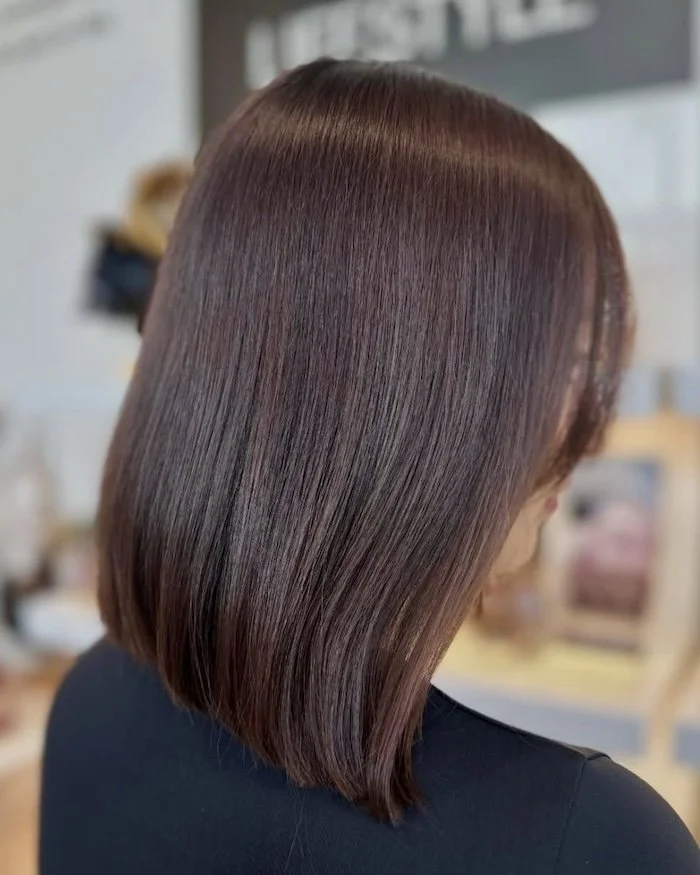 Side view of a woman with sleek, straight, shiny brown hair cut in a medium-length bob.