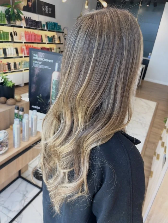 Back view of a woman's long, wavy hair with blonde highlights in a hair salon.