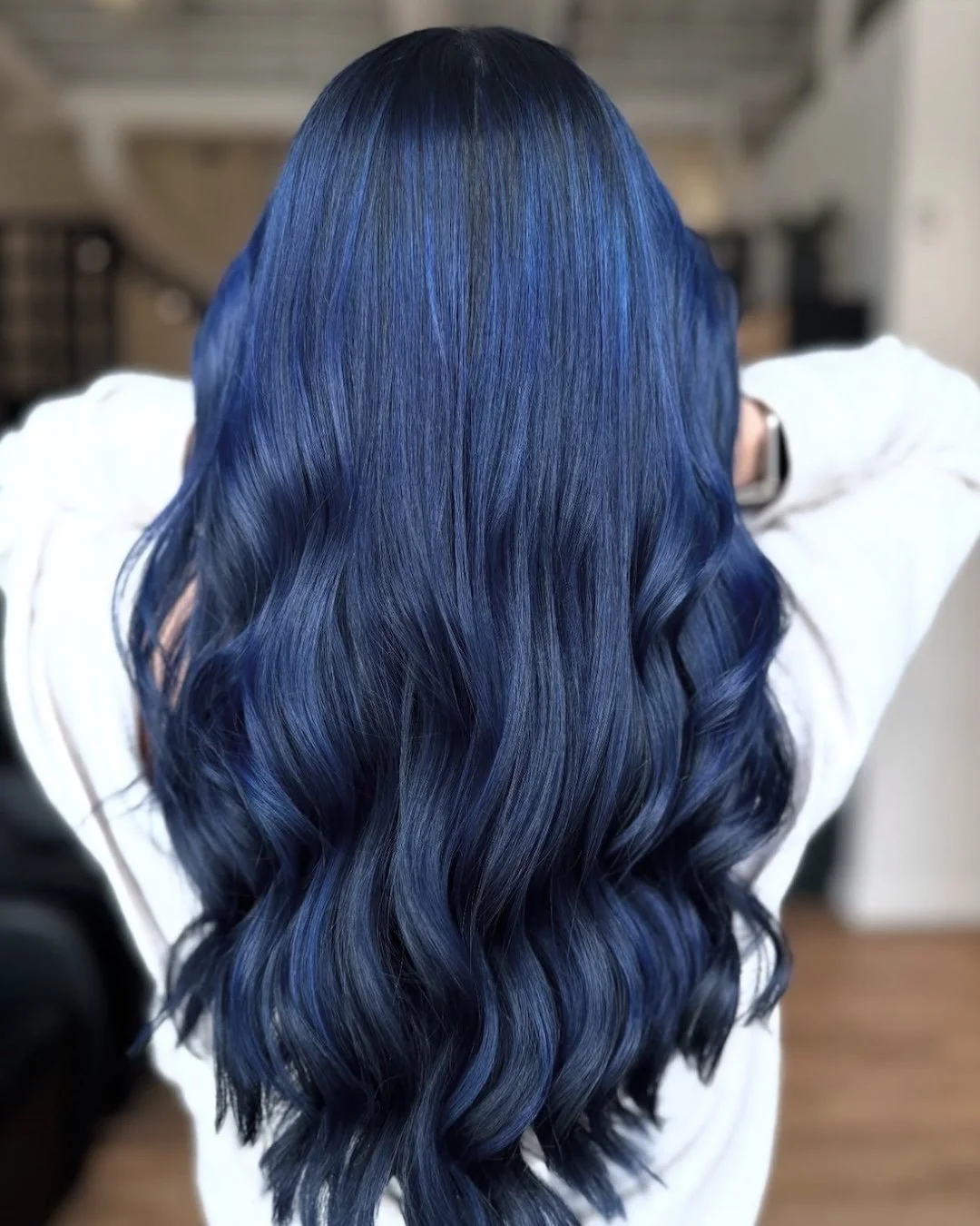 Back view of a person with long, wavy hair dyed in various shades of blue, from dark navy to bright cobalt, with soft curls.