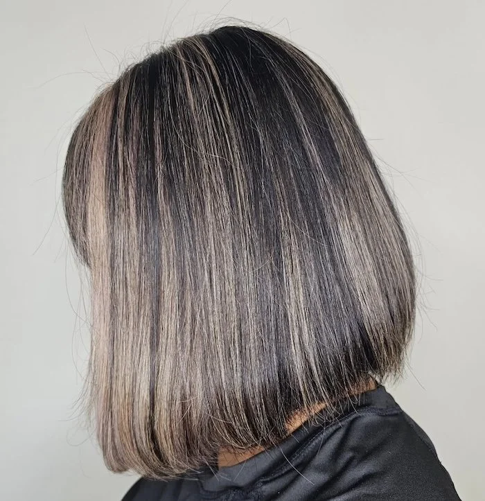 A person with shoulder-length straight hair dyed in shades of blonde, brown, and black, wearing a black top.