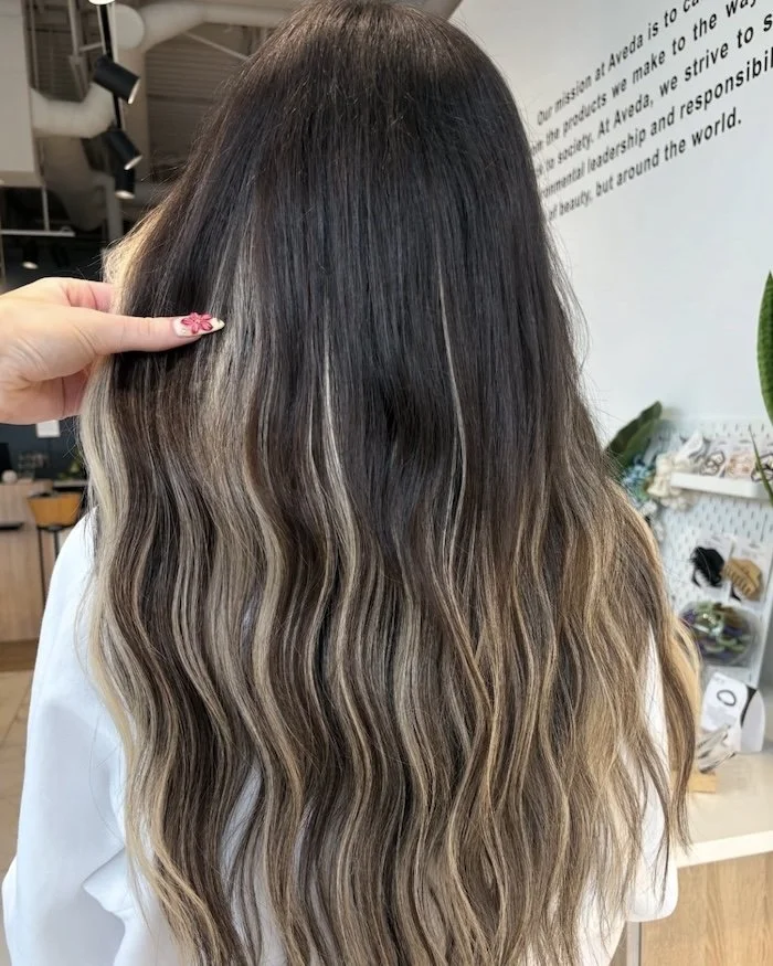 Close-up of a woman’s long, wavy hair with dark roots gradually transitioning to lighter blonde highlights.