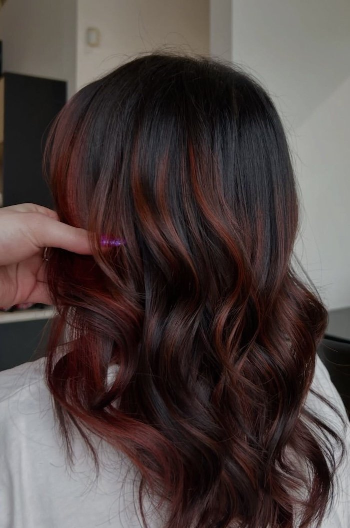 Back view of a woman's hair with a dark base color and red highlights in loose waves.