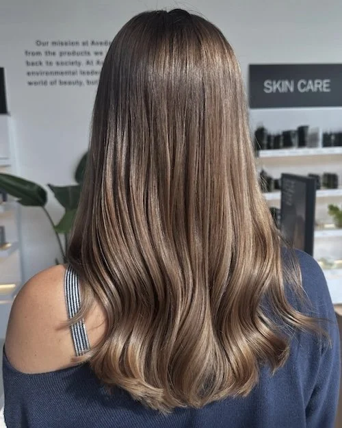 Back of a woman with long, wavy, light brown hair in a retail beauty store, with a 'Skin Care' sign in the background.