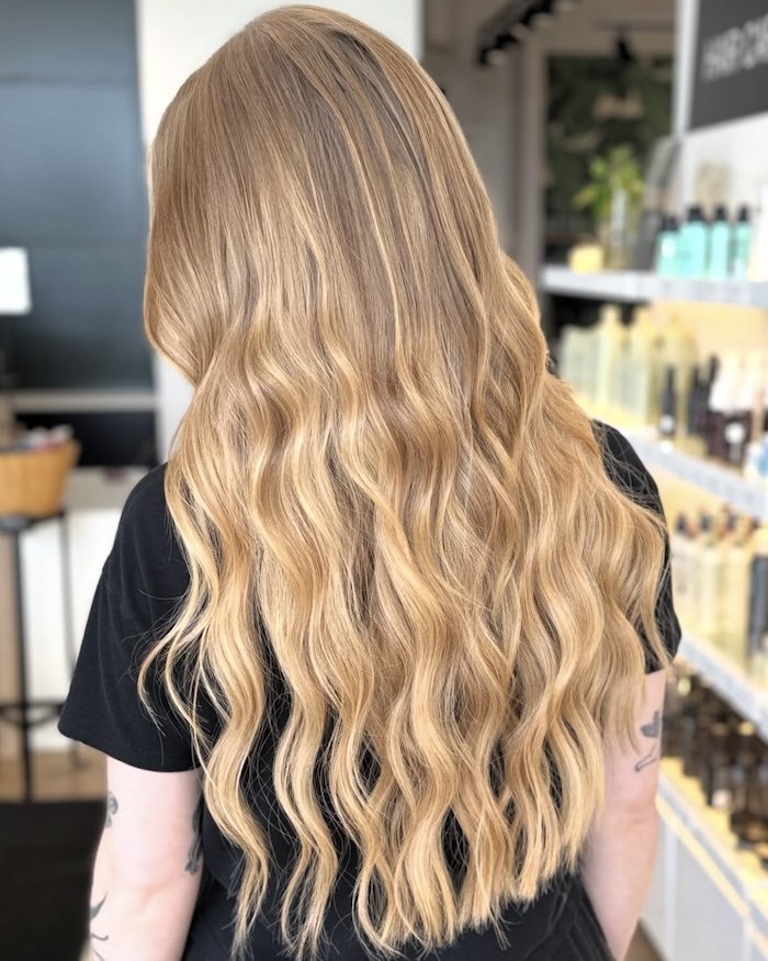 A woman with long, wavy blonde hair viewed from behind in a store or salon.