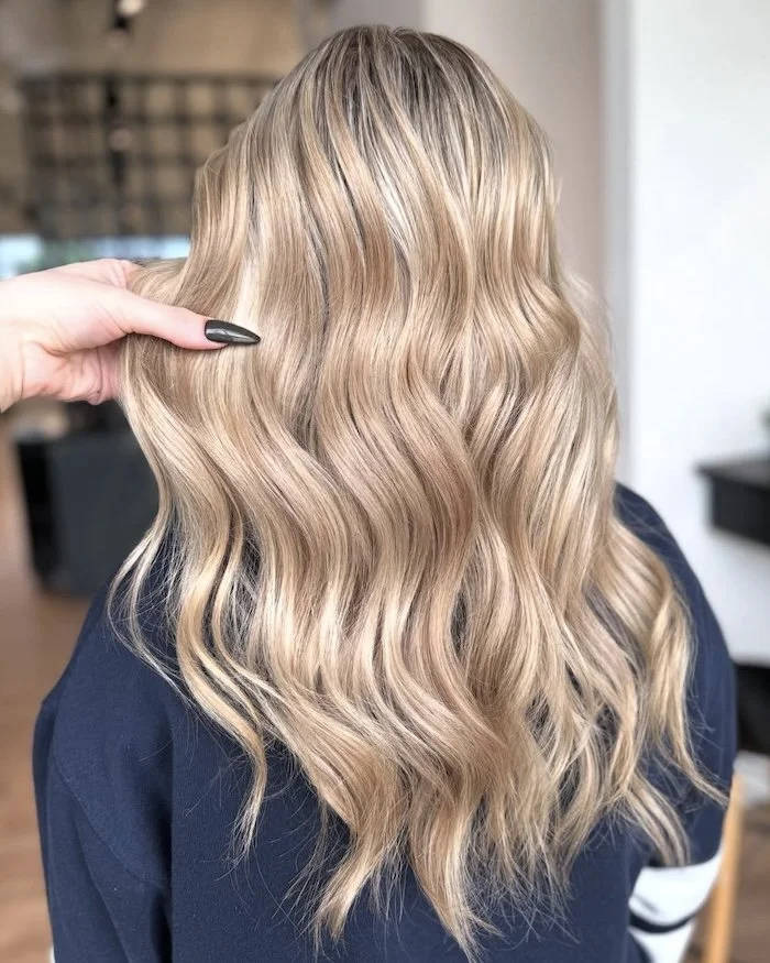 A woman with long, wavy blonde hair being styled or examined in a salon setting.