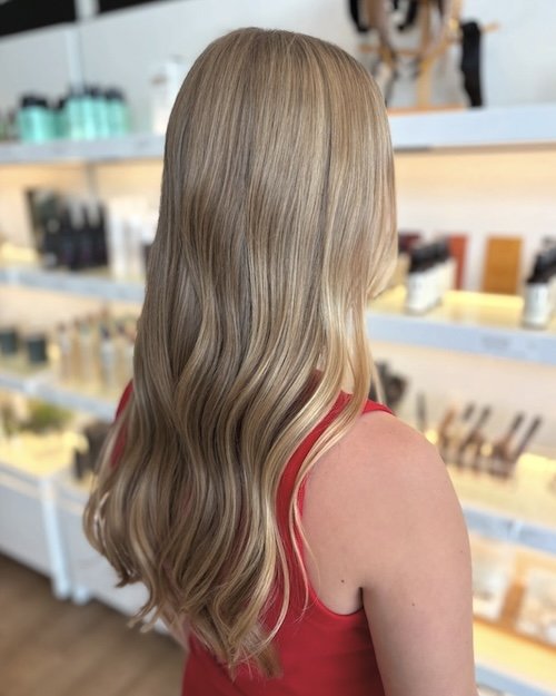 Side view of a woman with long, wavy blonde hair wearing a red top in a beauty store or salon.