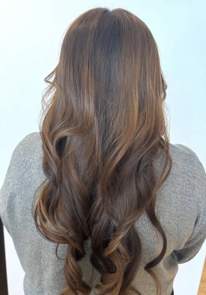 Back view of a woman with long, wavy, light brown hair wearing a gray sweater