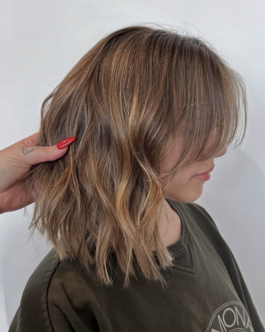 A woman with shoulder-length wavy hair being held by a hand with red nail polish, against a plain background.
