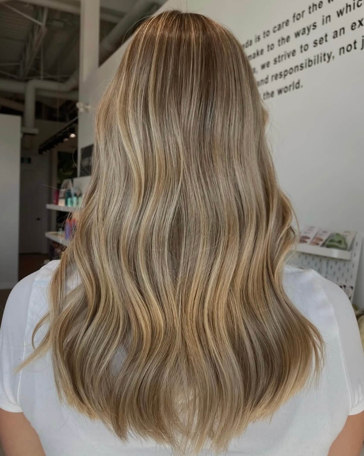 Back view of a person with long, wavy blonde hair in a salon.